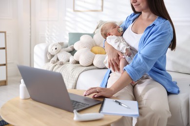 Photo of Telehealth. Mother with her baby having online consultation with doctor on sofa indoors, closeup