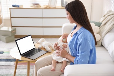 Photo of Telehealth. Mother with her baby having online consultation with doctor on sofa indoors