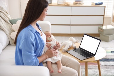 Photo of Telehealth. Mother with her baby having online consultation with doctor on sofa indoors