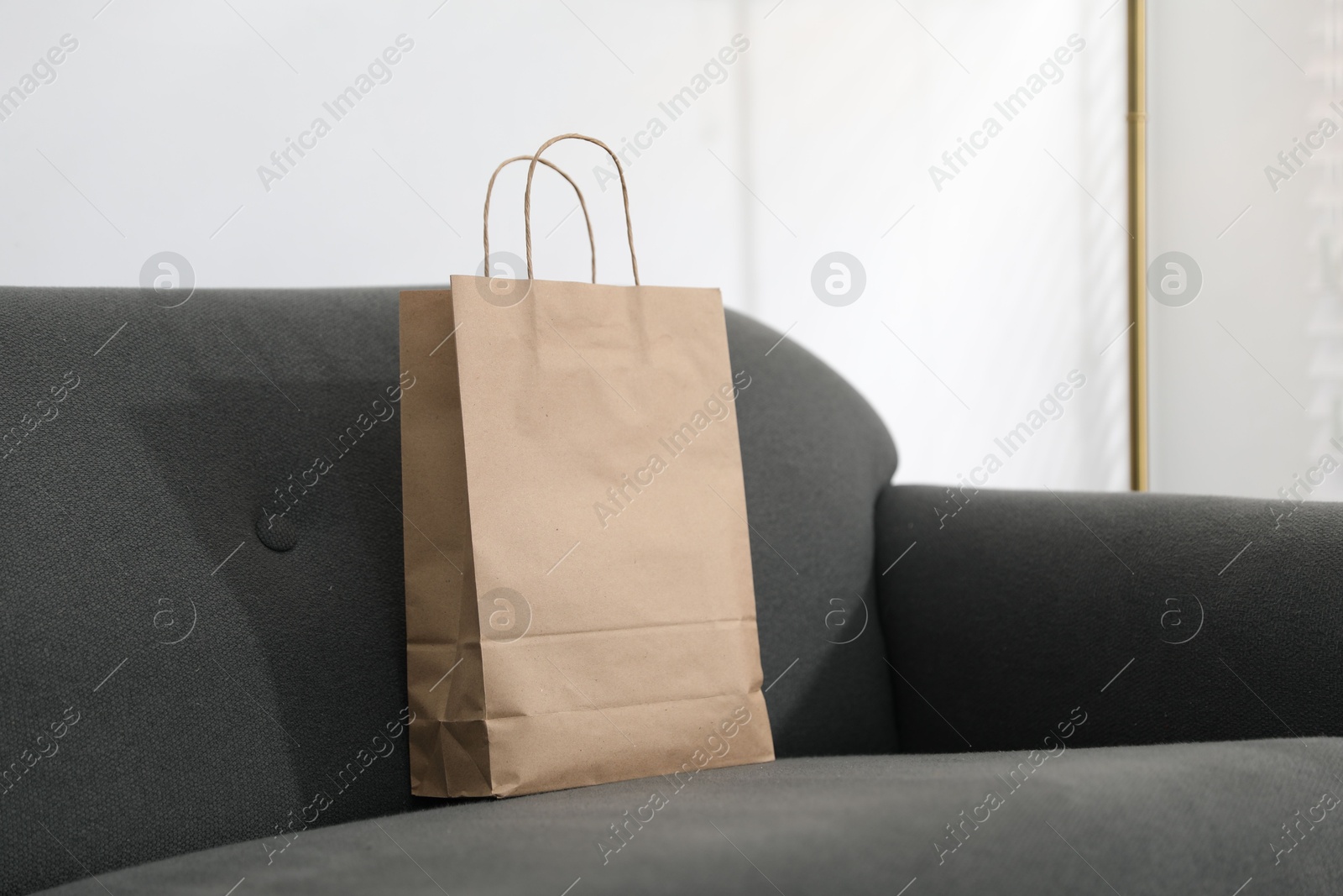 Photo of Paper bag on grey sofa indoors. Space for text