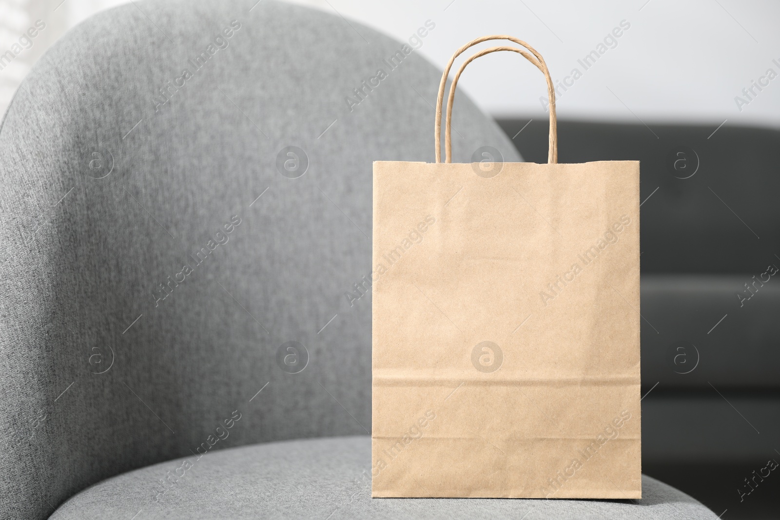 Photo of Paper bag on grey armchair indoors, closeup. Space for text