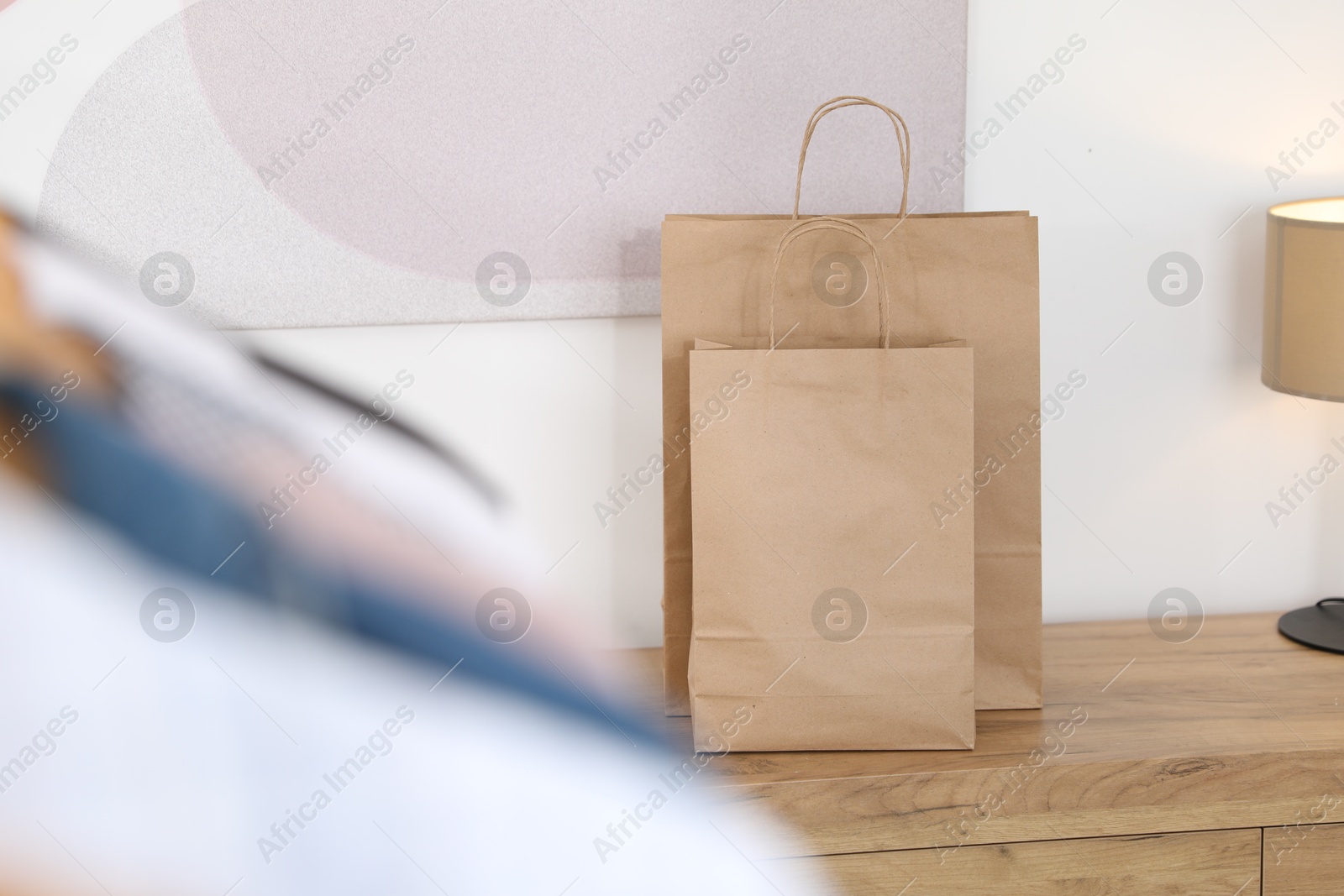 Photo of Paper bags on wooden chest of drawers near white wall indoors