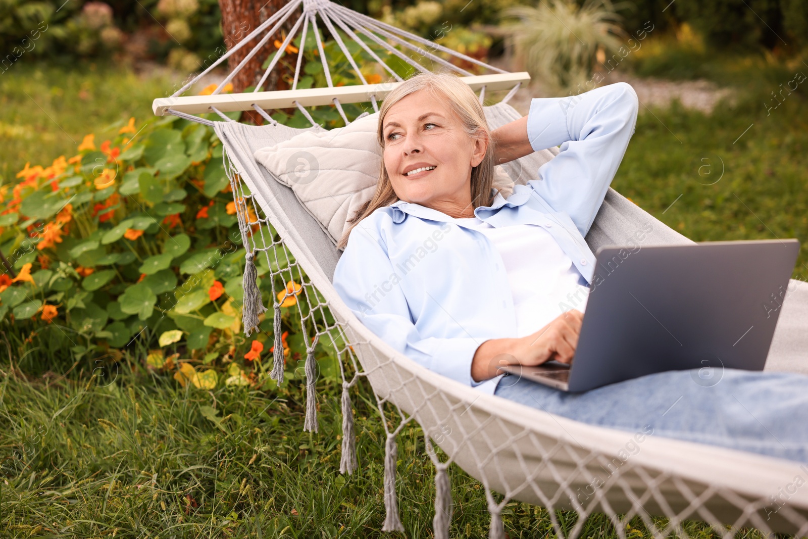 Photo of Senior woman with laptop in hammock outdoors