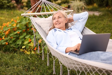 Photo of Senior woman with laptop in hammock outdoors
