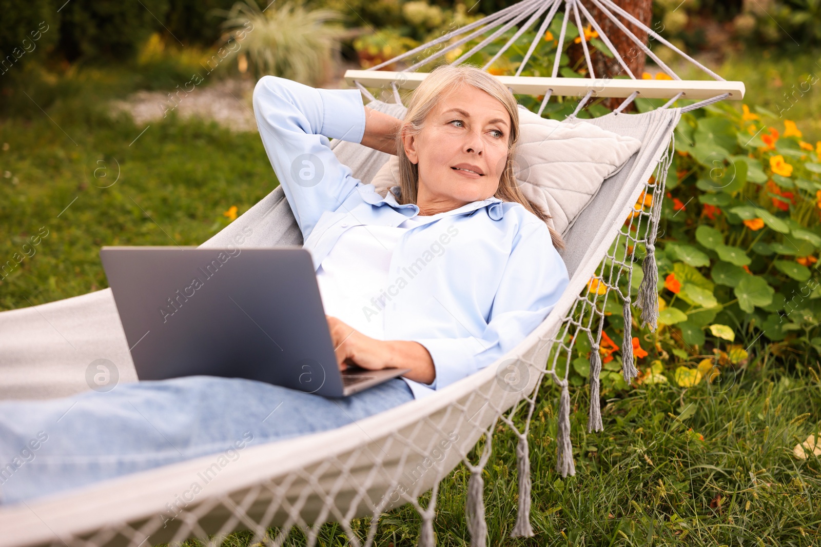 Photo of Senior woman with laptop in hammock outdoors