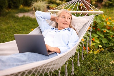 Photo of Senior woman with laptop in hammock outdoors