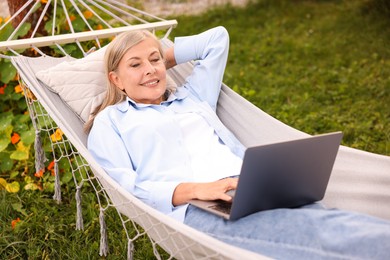 Photo of Senior woman with laptop in hammock outdoors