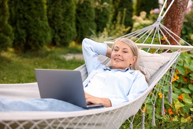 Photo of Senior woman with laptop in hammock outdoors