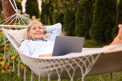 Photo of Senior woman with laptop in hammock outdoors