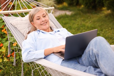 Photo of Senior woman with laptop in hammock outdoors
