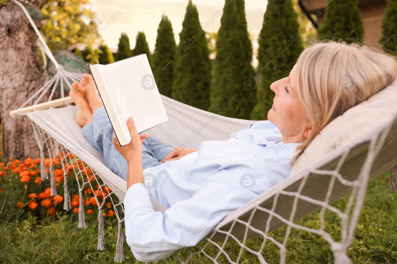 Photo of Senior woman reading book in hammock outdoors