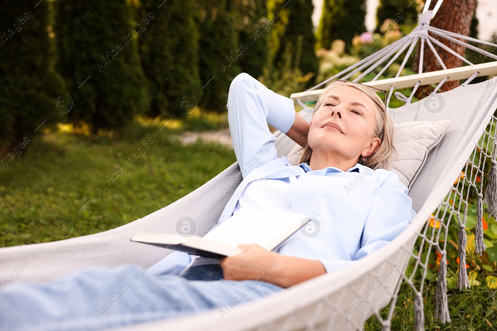 Photo of Senior woman with book resting in hammock outdoors