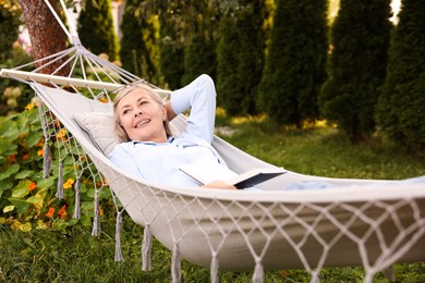 Photo of Senior woman with book resting in hammock outdoors