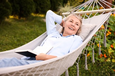Photo of Senior woman with book resting in hammock outdoors