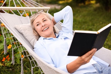 Photo of Senior woman with book resting in hammock outdoors