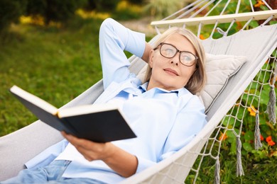 Photo of Senior woman with book resting in hammock outdoors