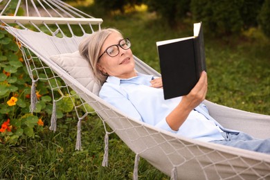 Photo of Senior woman reading book in hammock outdoors