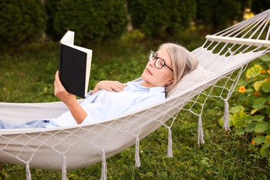 Photo of Senior woman reading book in hammock outdoors