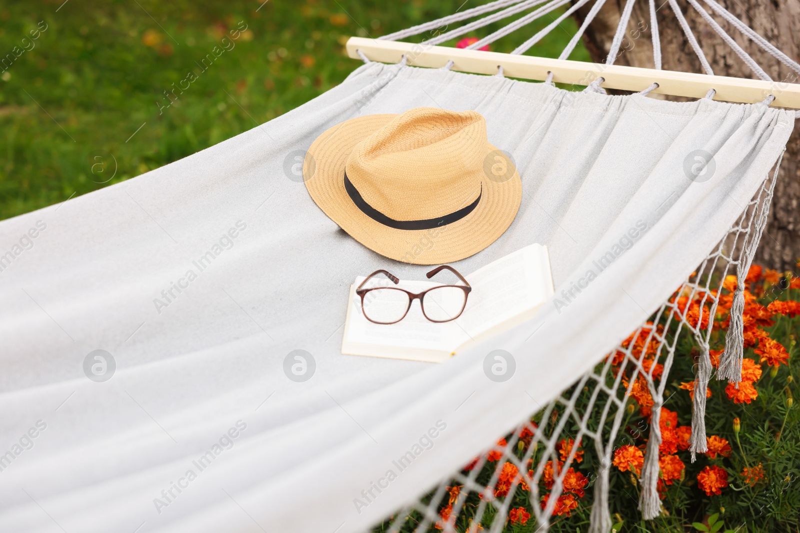Photo of Straw hat, glasses and book on hammock outdoors