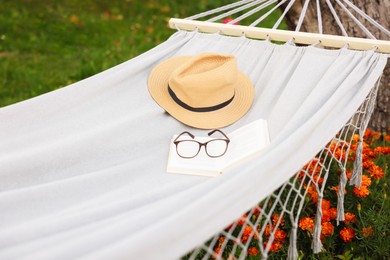 Photo of Straw hat, glasses and book on hammock outdoors