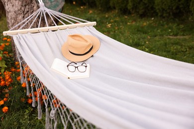 Photo of Straw hat, glasses and book on hammock outdoors