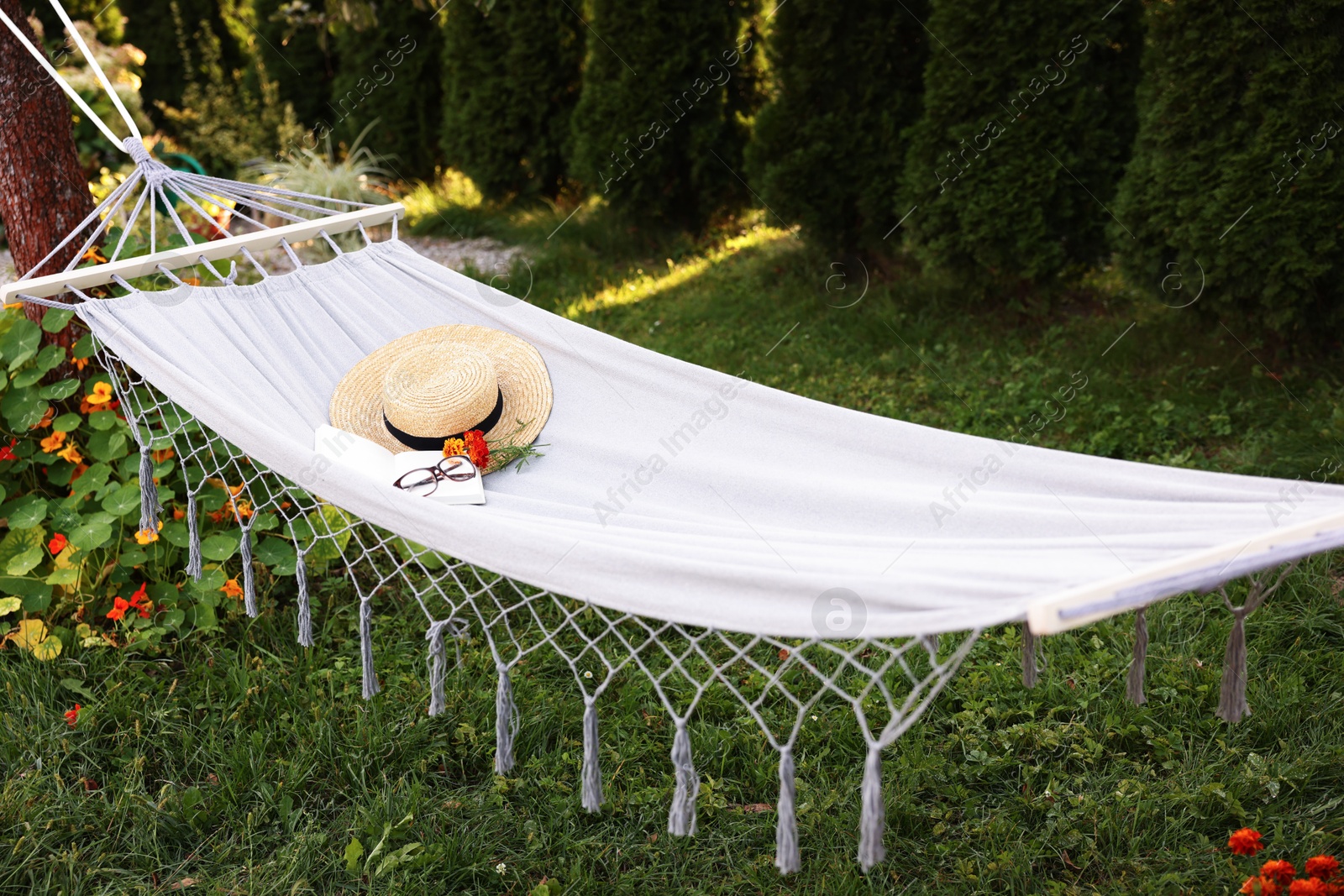Photo of Straw hat, glasses, book and flowers on hammock outdoors
