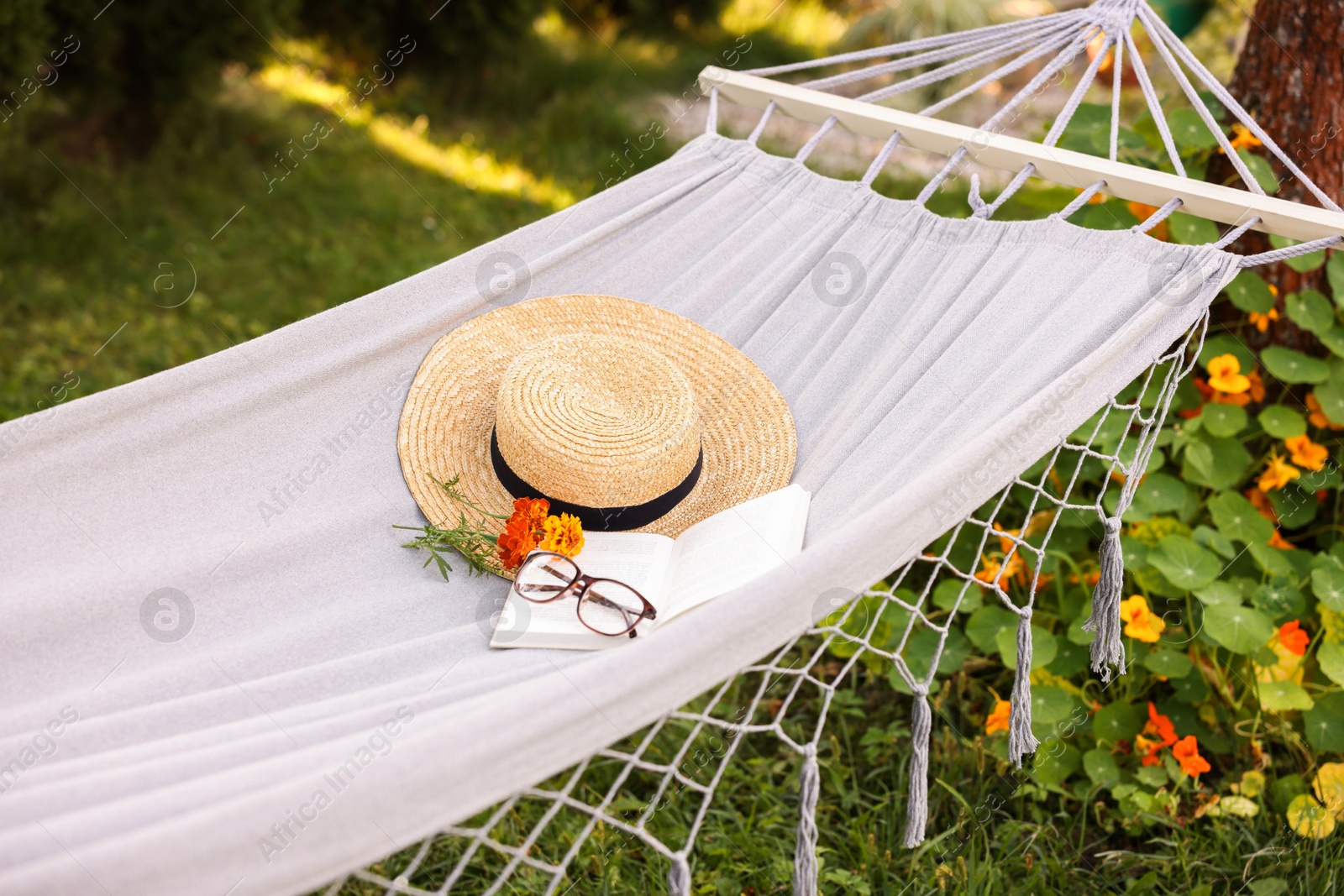 Photo of Straw hat, glasses, book and flowers on hammock outdoors