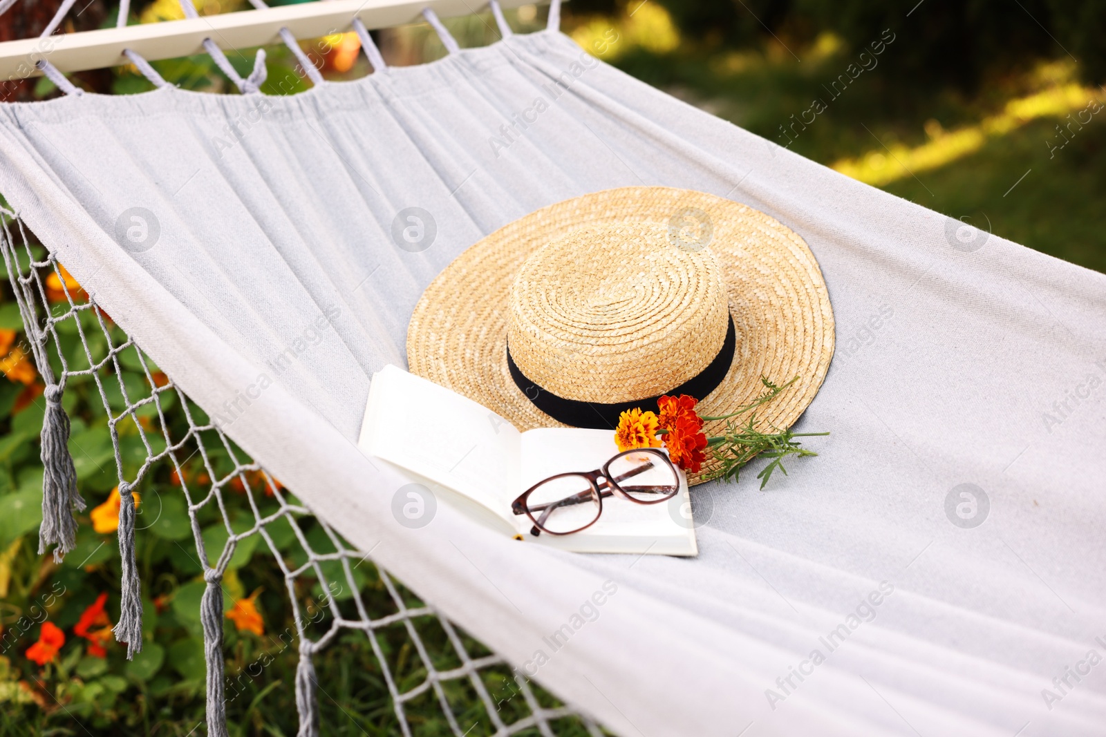 Photo of Straw hat, glasses, book and flowers on hammock outdoors