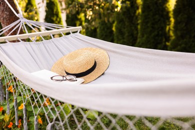 Photo of Straw hat, glasses and book on hammock outdoors