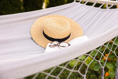 Photo of Straw hat, glasses and book on hammock outdoors
