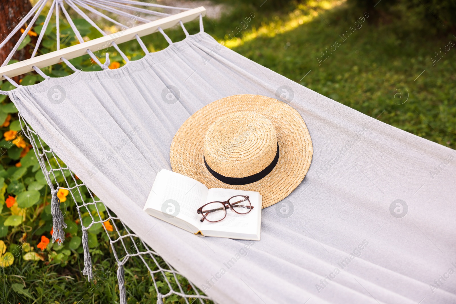 Photo of Straw hat, glasses and book on hammock outdoors