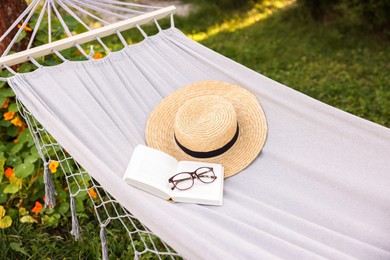 Photo of Straw hat, glasses and book on hammock outdoors