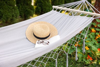 Photo of Straw hat, glasses and book on hammock outdoors