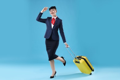 Photo of Positive stewardess with suitcase on light blue background