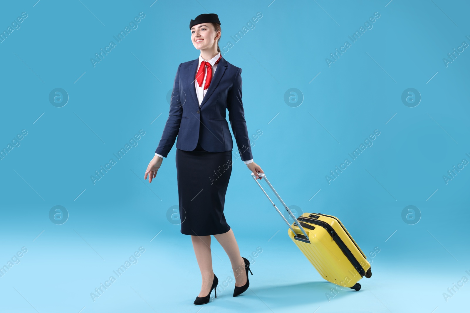 Photo of Positive stewardess with suitcase on light blue background
