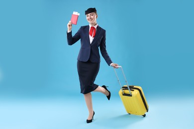 Photo of Positive stewardess with suitcase, passport and tickets on light blue background