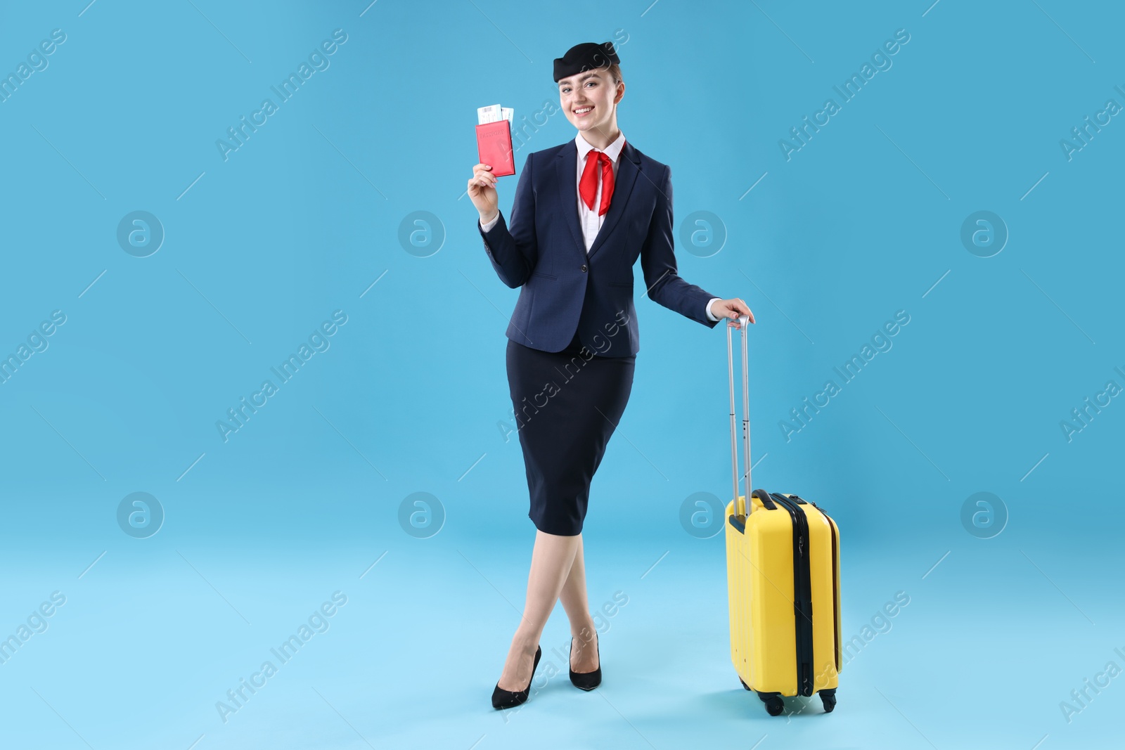 Photo of Positive stewardess with suitcase, passport and tickets on light blue background