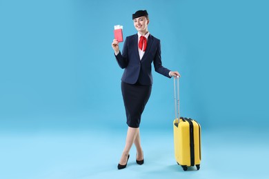 Photo of Positive stewardess with suitcase, passport and tickets on light blue background