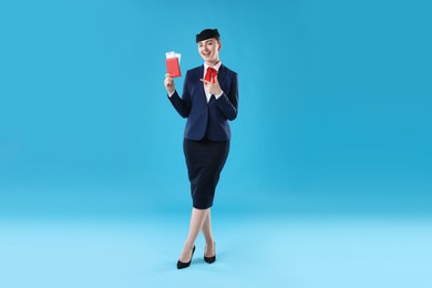 Photo of Smiling stewardess pointing at passport and tickets on light blue background