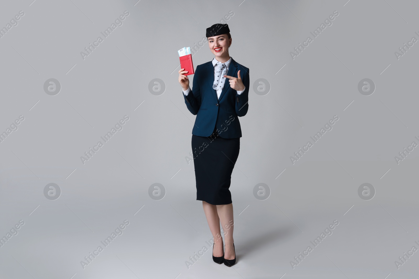Photo of Smiling stewardess pointing at passport and tickets on light grey background