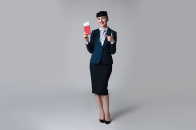 Photo of Smiling stewardess pointing at passport and tickets on light grey background