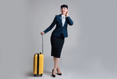 Photo of Positive stewardess with suitcase on light grey background