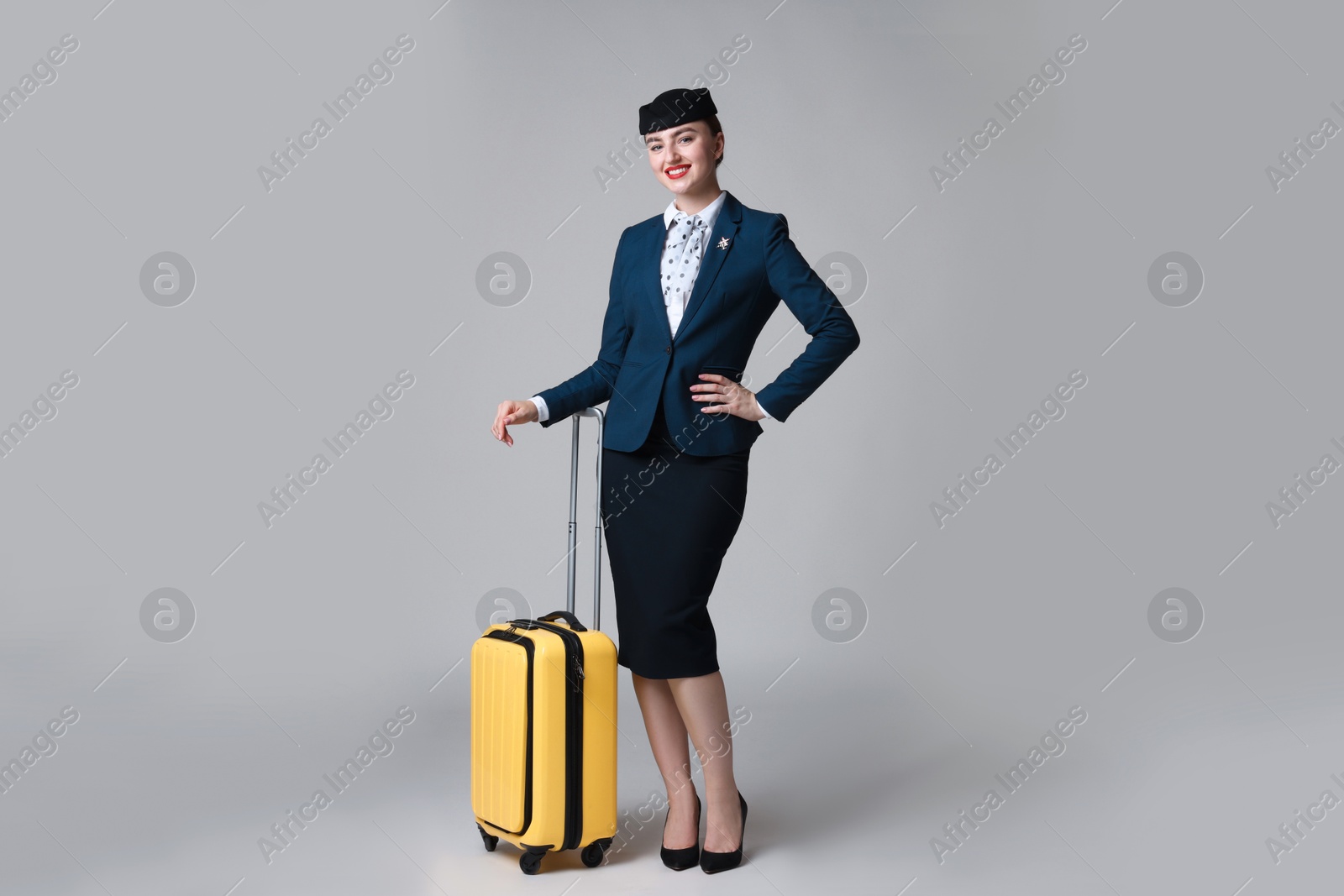 Photo of Positive stewardess with suitcase on light grey background