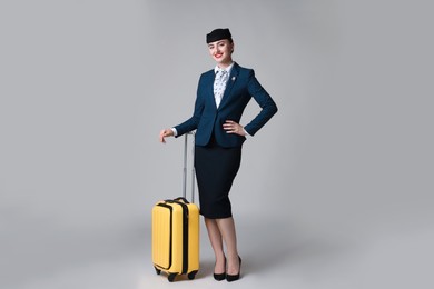 Photo of Positive stewardess with suitcase on light grey background