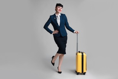 Photo of Positive stewardess with suitcase on light grey background