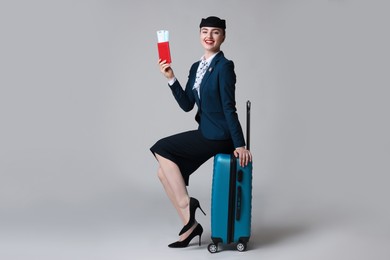 Photo of Positive stewardess with suitcase, passport and tickets on light grey background
