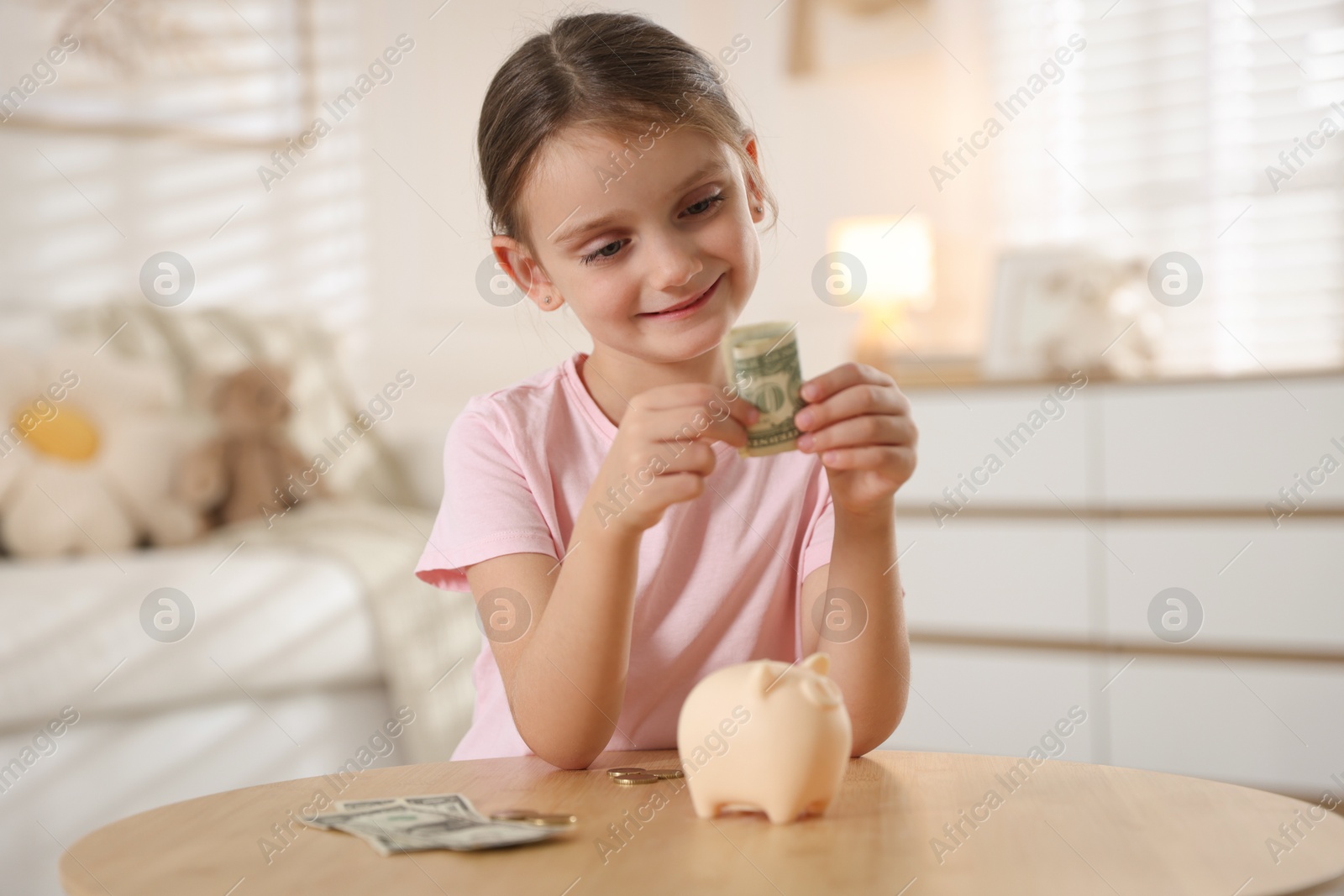 Photo of Little girl with pocket money and piggy bank at wooden table indoors