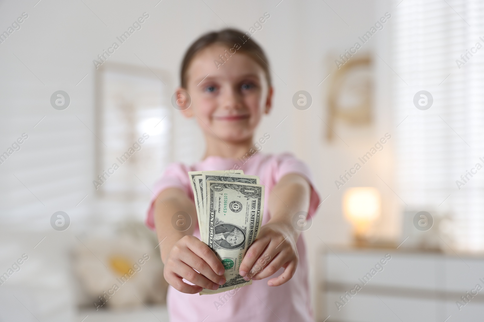 Photo of Little girl holding pocket money at home, selective focus