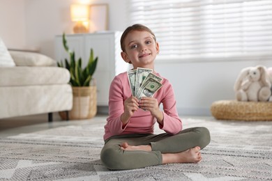 Photo of Little girl holding pocket money on floor at home
