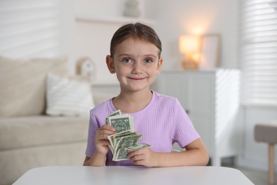 Photo of Little girl holding pocket money at white table indoors